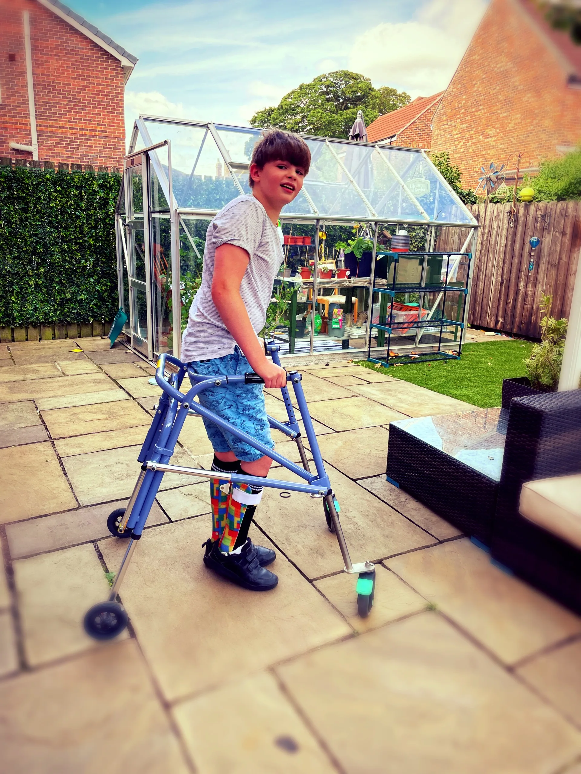 Lucas in his garden with his walking frame and greenhouse behind him